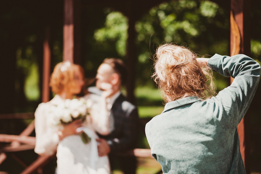 Fotograf robi zdjęcie młodej parze w drewnianej, ogrodowej altanie. Ujęcie zza pleców fotografa