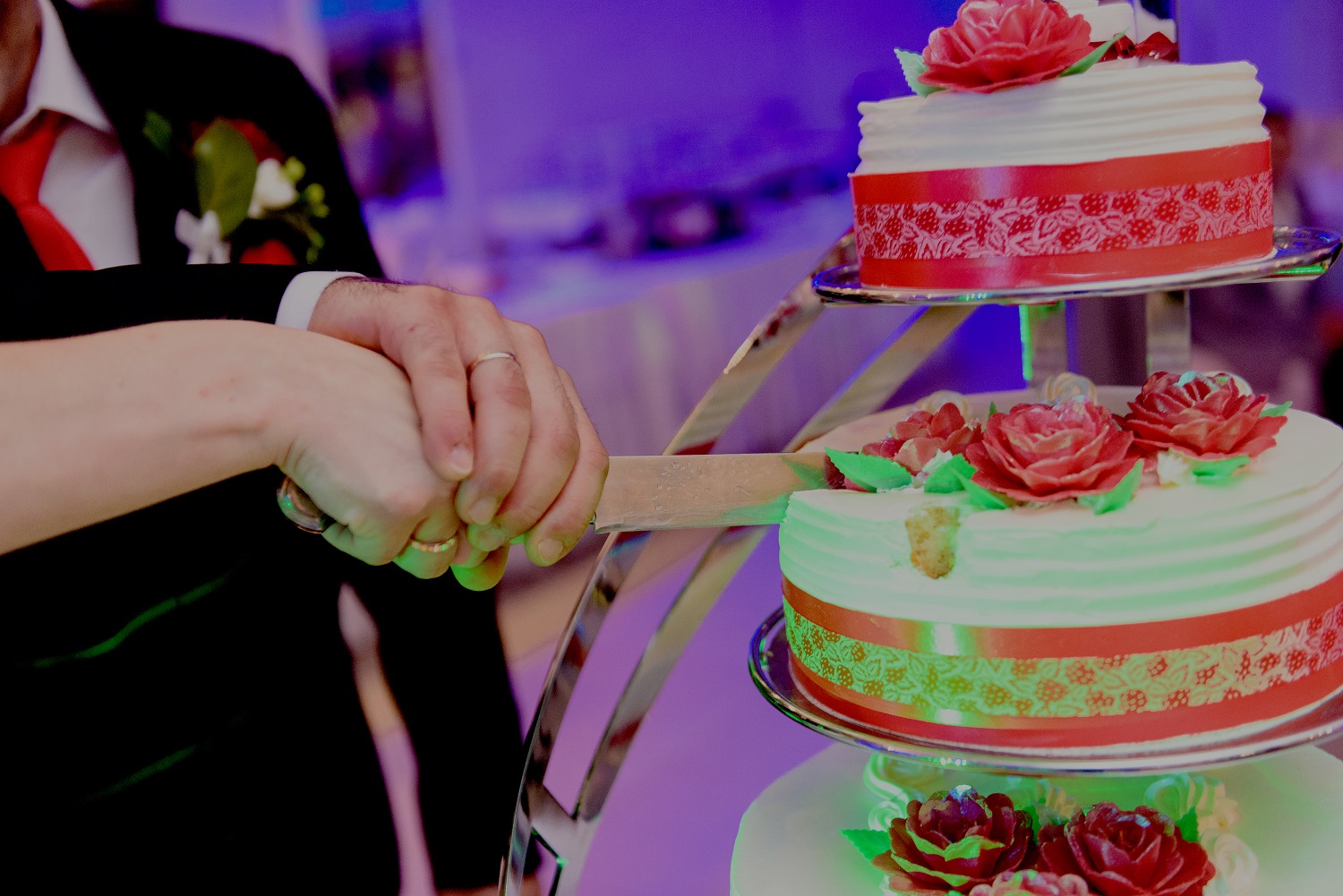 Para młoda kroi tort weselny - pani młoda trzyma nóż, a pan młody obejmuje jej dłoń